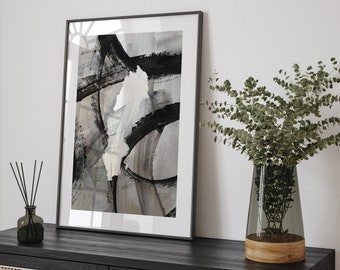 May include: A black framed print with an abstract design in shades of gray and black. The print is hanging on a white wall above a black dresser with a wooden top. A vase with green leaves is on the dresser.