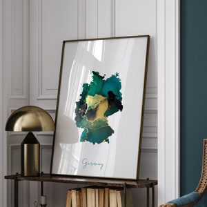 Op de afbeelding: Een ingelijste print van een abstracte kaart van Duitsland in tinten groen, turquoise en goud. Het woord "Duitsland" staat in cursief onderaan de print.