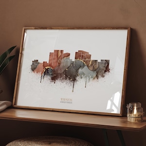 May include: A framed art print featuring a watercolor skyline design. The artwork showcases a cityscape in shades of brown, gray, and gold, with the text "WHEATON UNITED STATES" at the bottom. The print is displayed in a wooden frame.