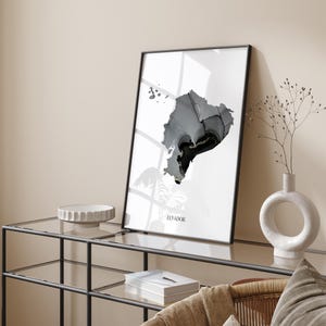 May include: A black and white minimalist art print of the outline of Ecuador. The print is framed in a black frame and is hanging on a wall above a glass shelf.