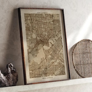 Puede incluir: Un mapa enmarcado de Perth, Australia, en tonos sepia. El mapa detalla el diseño de la ciudad, incluidas las calles y vías fluviales. El marco es de color marrón oscuro, y el texto "PERTH, AUSTRALIA" es visible en la parte inferior.