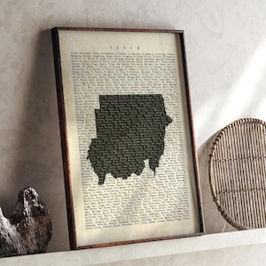Könnte beinhalten: Gerahmter Druck mit einer Karte des Sudan in dunkler Silhouette vor einem Hintergrund im Vintage-Stil, der mit Text gefüllt ist. Der Rahmen ist dunkelbraun, und der Druck wird auf einem weißen Regal präsentiert.