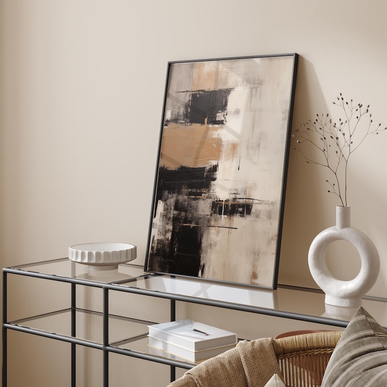 May include: Abstract art print in black, white, and brown tones framed in a black frame. The print is displayed on a glass shelf with a white bowl and a white vase with a circular opening.