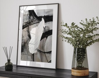 May include: A black framed print with abstract black and white brushstrokes on a gray background. The print is hanging on a white wall above a black wooden cabinet with a woven rattan front.