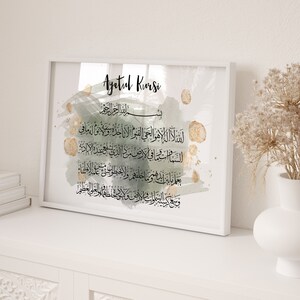 Może przedstawiać: Wydruk w ramie z białym tłem i zielono-złotym wzorem akwarelowym. Wydruk zawiera arabski tekst Ayatul Kursi, wersetu z Koranu.
