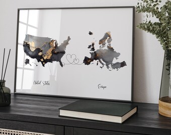 May include: A black and white map with gold accents showing the United States and Europe connected by a line with two hearts. The text "United States" and "Europe" is below each continent. The map is framed in a black frame and is hanging on a wall.
