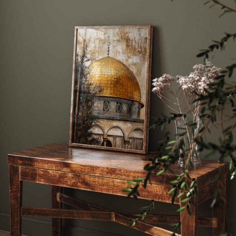 May include: A framed print of a golden dome mosque with a brown wooden frame. The print is on a wooden table with a green plant in the foreground.