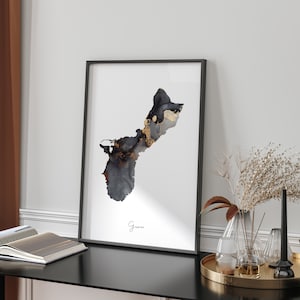 May include: A black and gold abstract art print of the island of Guam. The print is framed in a black frame and is hanging on a white wall.