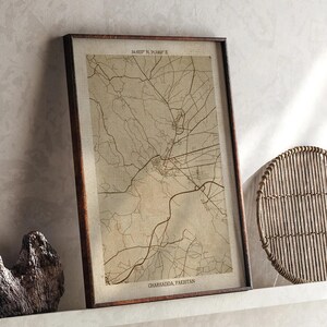 May include: A framed sepia-toned map print of Charsadda, Pakistan. The map shows detailed roads and geographical features, with coordinates at the top and the city name at the bottom. The frame is dark brown.