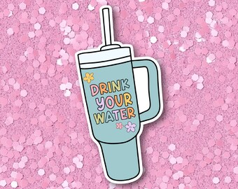 May include: A blue and white tumbler with a straw and the text "DRINK YOUR WATER" in colorful letters. The tumbler has a handle and is decorated with small flowers.