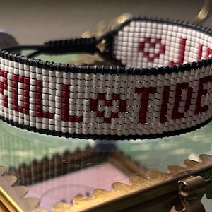 May include: White beaded bracelet with black thread and red lettering that reads "ALL THE TIME".