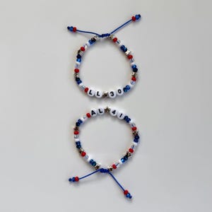 May include: Two adjustable bracelets featuring red, white, and blue beads, silver star-shaped spacers, and white letter beads. One bracelet displays the text LL 30, while the other displays the text AL 41, both strung on blue cord.