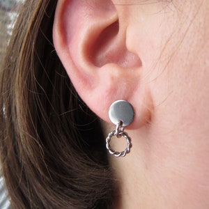 May include: Silver earrings with a small round disc and a twisted hoop dangling below.