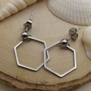 May include: A pair of silver hexagon hoop earrings with a smooth, rounded ball at the top of each earring.