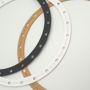 May include: Close-up of three circular decorative elements. One is black, one is white, and one is tan. Each ring has a series of small, evenly spaced cut-out shapes. The rings overlap slightly against a white background.
