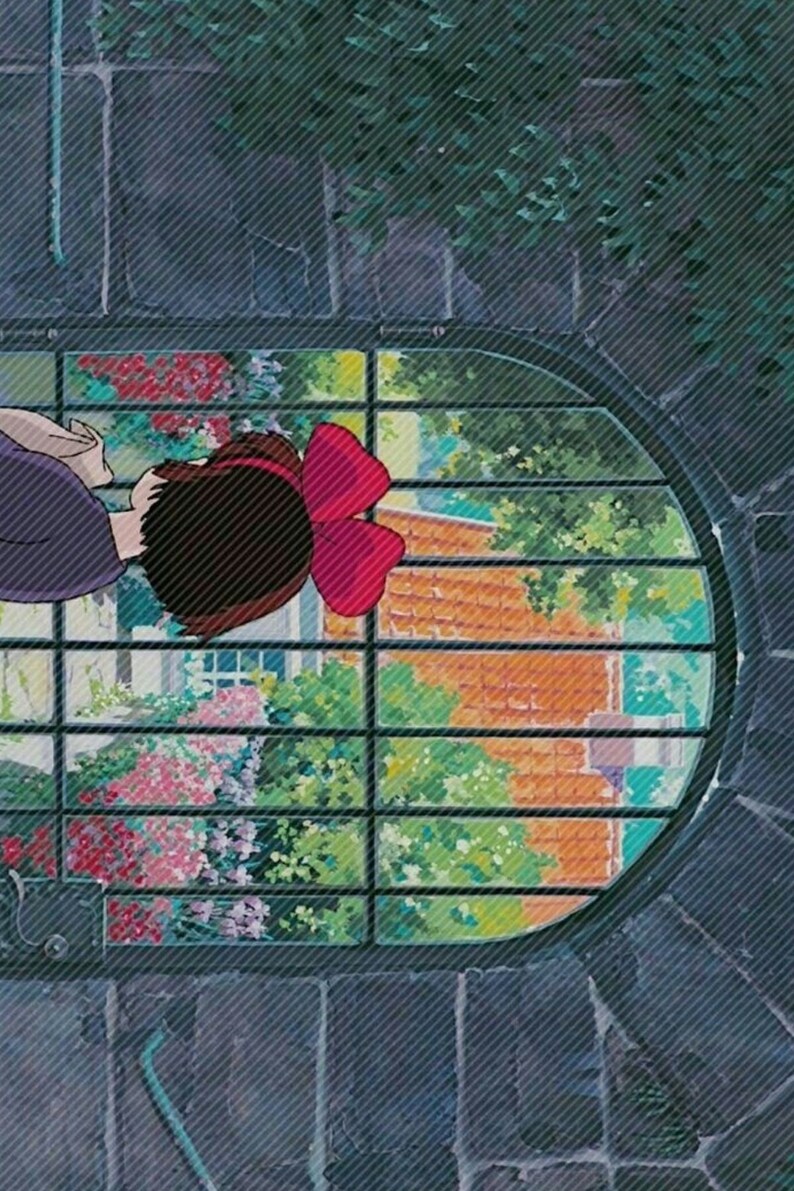 May include: A young girl with brown hair and a red bow looks out a window with a barred, oval frame. The window shows a view of a brick building with green foliage and flowers.