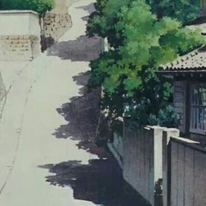 May include: A narrow, winding street in a Japanese neighborhood. The street is lined with traditional houses and lush green trees. The houses have white walls and brown roofs. The street is paved with gray concrete and has a slight incline.