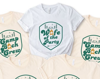 May include: Four beige t-shirts with green and orange graphics. The shirts feature a retro-style design with a shield shape and the text "Camp Boch Crew". One white t-shirt features a green shield with the text "Wife of the Party".