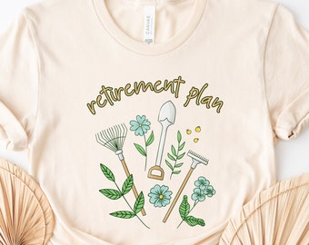 May include: A beige t-shirt with the text "retirement plan" in gold lettering. The design features gardening tools and flowers.
