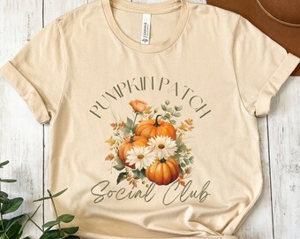May include: A beige t-shirt with a graphic design of pumpkins, flowers, and leaves. The text "Pumpkin Patch Social Club" is printed on the shirt.