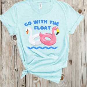 May include: A light blue t-shirt with the text "Go with the float" printed on it. The text is surrounded by a white swan and a pink flamingo pool float.