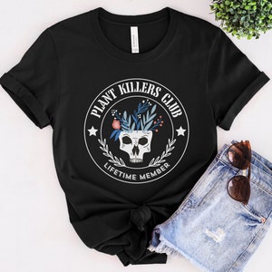 May include: Black t-shirt with a white circle graphic featuring a skull with flowers on top. The text inside the circle reads "Plant Killers Club Lifetime Member".