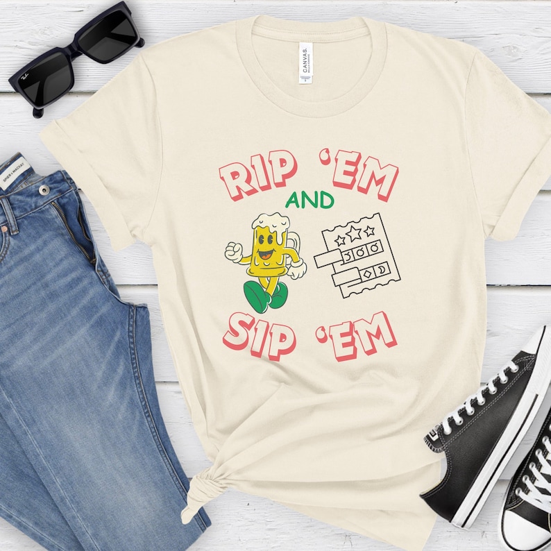 May include: A beige t-shirt with the text "Rip 'Em and Sip 'Em" in pink and green letters. A cartoon beer mug with a face is holding a ticket with stars and numbers.