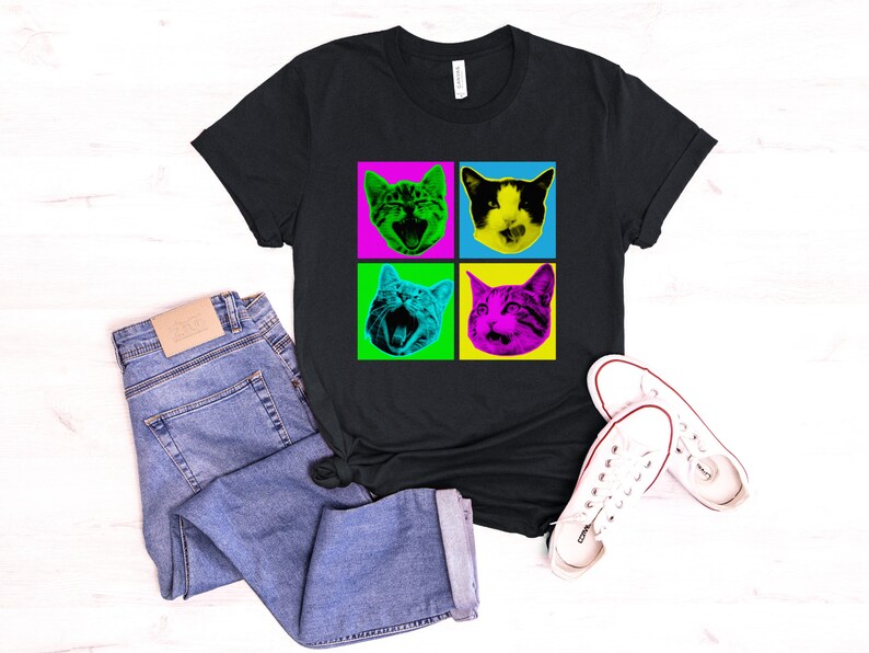 May include: Black t-shirt with a pop art design of four cats with different colored backgrounds. The cats are all looking at the camera with their mouths open.