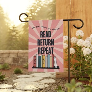 May include: A pink garden flag with a sunburst design and the text "the best books are shared! READ RETURN REPEAT". A row of colorful books are on a shelf below the text.