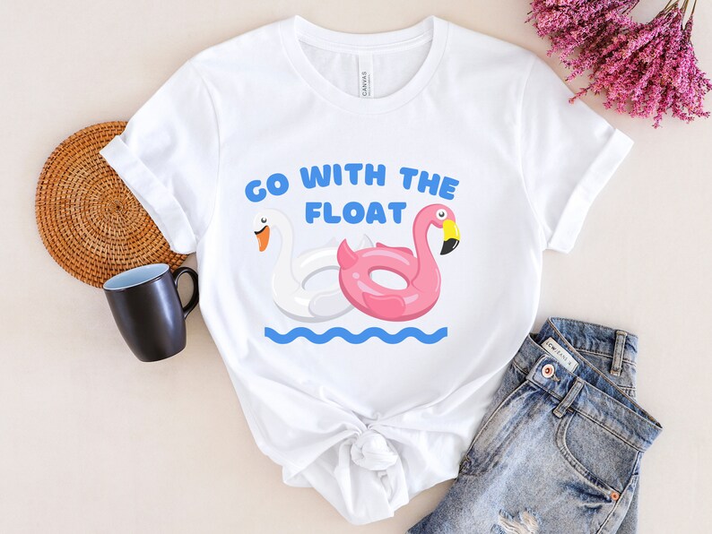 May include: White t-shirt with a graphic of a pink flamingo and white swan pool float. The text "Go with the float" is printed on the shirt.