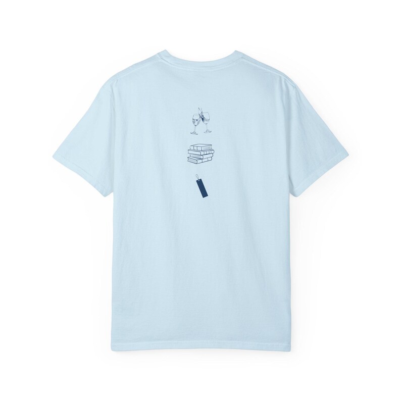 Op de afbeelding: Lichtblauw T-shirt met een afbeelding van een stapel boeken, een glas wijn en een bladwijzer.