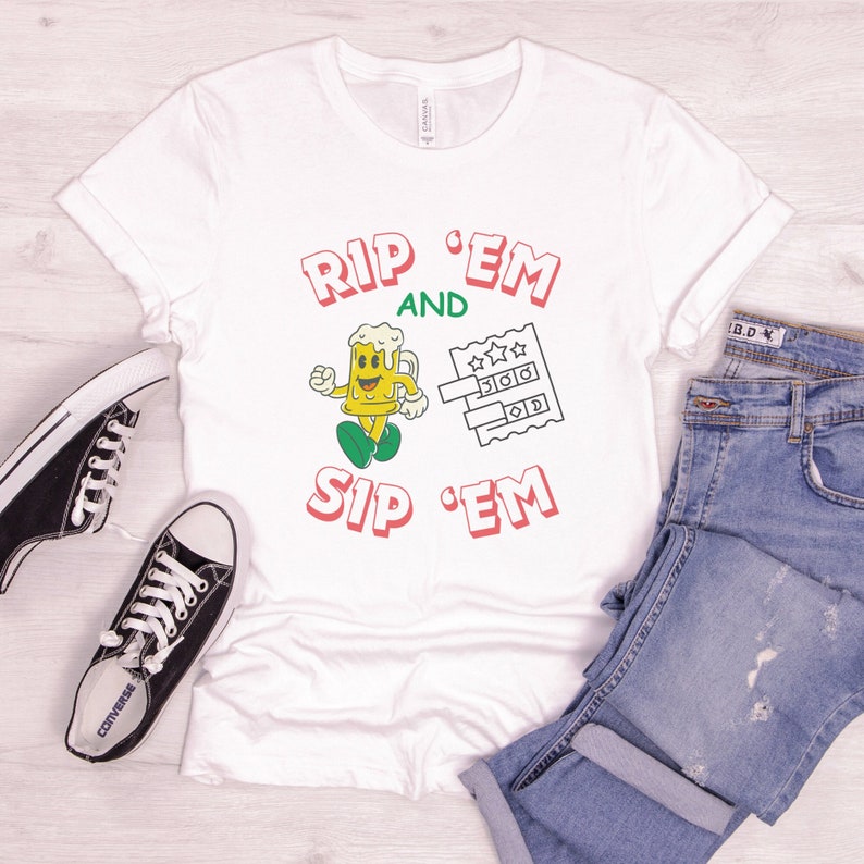 May include: White t-shirt with red and green text that says "Rip 'Em and Sip 'Em". A cartoon beer mug with a smiling face is holding a beer glass and walking to the right. A green and white bingo card is to the right of the beer mug.