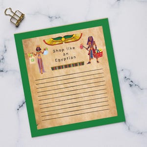 May include: A green-edged notepad featuring the text "Shop like an Egyptian" and Egyptian-themed illustrations. The notepad sits on a white marble surface, with a keyboard, coffee, and pencils nearby.