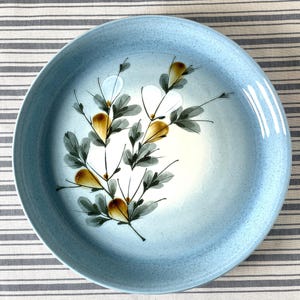 Può includere: Un piatto da portata in ceramica blu con un motivo floreale bianco e giallo. Il piatto ha una glassa macchiettata e un bordo leggermente rialzato.