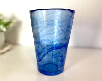 Può includere: Un bicchiere di vetro blu con un design a spirale marmoreo. Il bicchiere ha una base trasparente e un bordo blu.