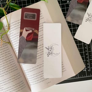 May include: Two bookmark designs. The first bookmark features a hand holding a glass of red liquid with a red background. The second bookmark features a crescent moon with floral accents and the text "Every End is a Beginning".