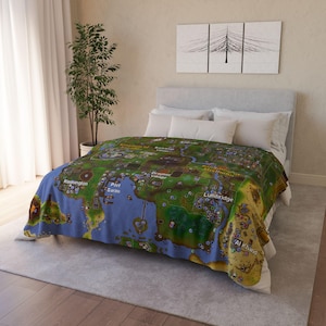 Puede incluir: Una manta con un mapa en azul, verde y amarillo, colocada sobre una cama. La manta presenta un diseño detallado del mapa con varias ubicaciones etiquetadas. La manta suave se coloca sobre una cama con almohadas blancas.