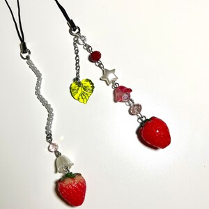 May include: Two phone charms with a strawberry, leaf, and beads. One charm has a white bell and the other has a star and pink flower.