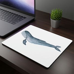 May include: A white mouse mat with a watercolour illustration of a blue whale. The whale is swimming to the right and has a white background.