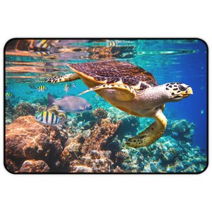 May include: A sea turtle swims through clear blue water with coral reefs and colourful fish in the background.