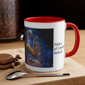 May include: A white ceramic mug with a red rim and handle. The mug features a colorful image of the Pillars of Creation Nebula with the text "Pillars of Creation Nebula" printed on the side.