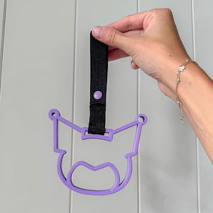 May include: A purple plastic keychain shaped like a cartoon character with a black strap and a purple button.