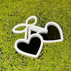 May include: Two white heart-shaped metal cutouts floating on a bed of green moss.
