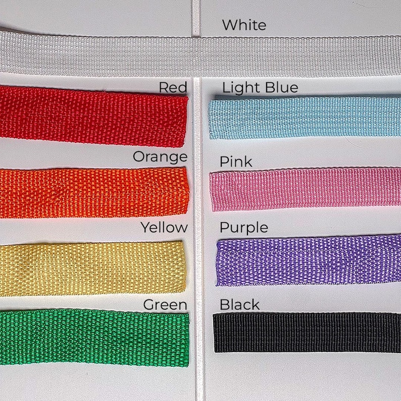 May include: A collection of colorful woven ribbons in various shades, including red, orange, yellow, green, light blue, pink, purple, black, and white. Each ribbon is labeled with its corresponding color name.