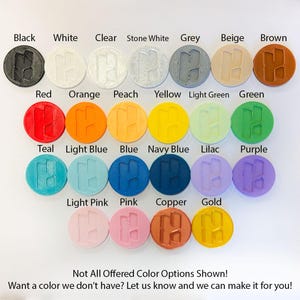 May include: A collection of round, colored objects, each with an "H" design, displayed against a white background. Colors include black, white, clear, grey, beige, brown, red, orange, peach, yellow, green, teal, light blue, blue, navy blue, lilac, purple, light pink, pink, copper, and gold. Text reads: "Not All Offered Color Options Shown! Want a color we don't have? Let us know and we can make it for you!"