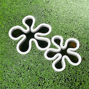 Peut inclure: Deux emportes-pièces en forme de fleur blanche avec des centres noirs, posés sur un lit de mousse verte.