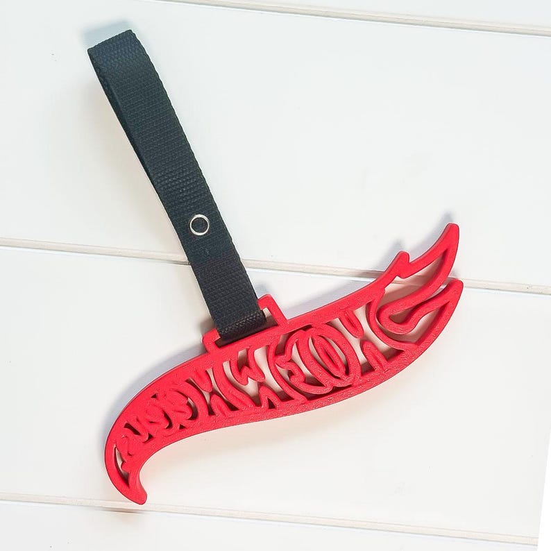 May include: A red, decorative, curved object with an intricate cutout design and a black strap with a metal grommet. The object is on a white surface.