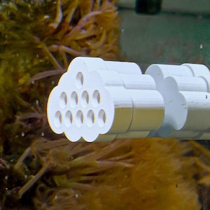 Puede incluir: Filtro de cerámica blanco con forma de nube y múltiples agujeros. El filtro está unido a una tubería de plástico blanco.