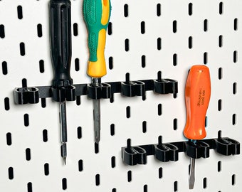 May include: Three screwdrivers in black holders attached to a white pegboard. The screwdrivers have black, green, and orange handles. The pegboard has evenly spaced holes. One screwdriver has the text "Snap-on SD02 USA".