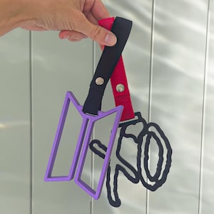 May include: A purple, geometric design and a black, stylized design are attached to black and red straps with silver snaps. The straps are held up against a light gray background.